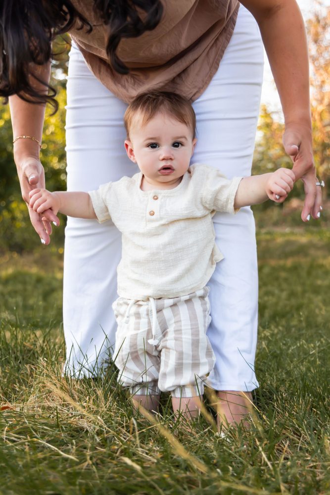 A baby boy standing with his mother's help during an outdoor family photography session in Cleveland, Ohio.