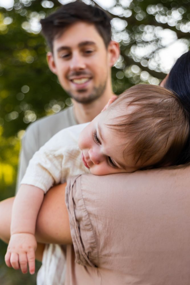 A smiling baby resting on his mother's shoulder during a warm, natural family photography session in Cleveland, Ohio.