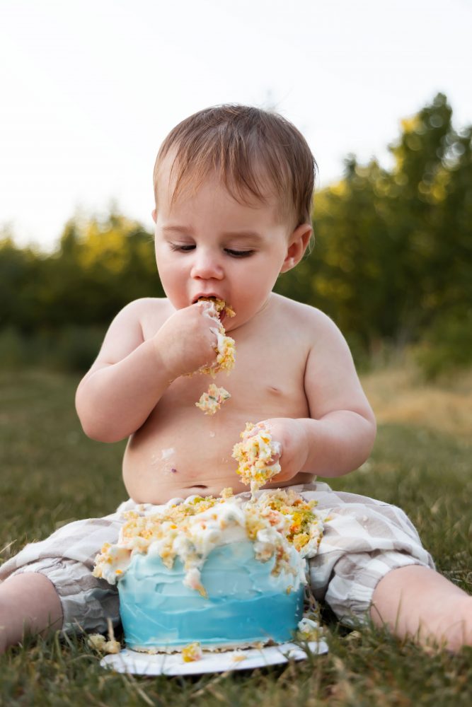 Cleveland cake smash photographer captures a laughing one-year-old covered in birthday cake frosting during an outdoor session.