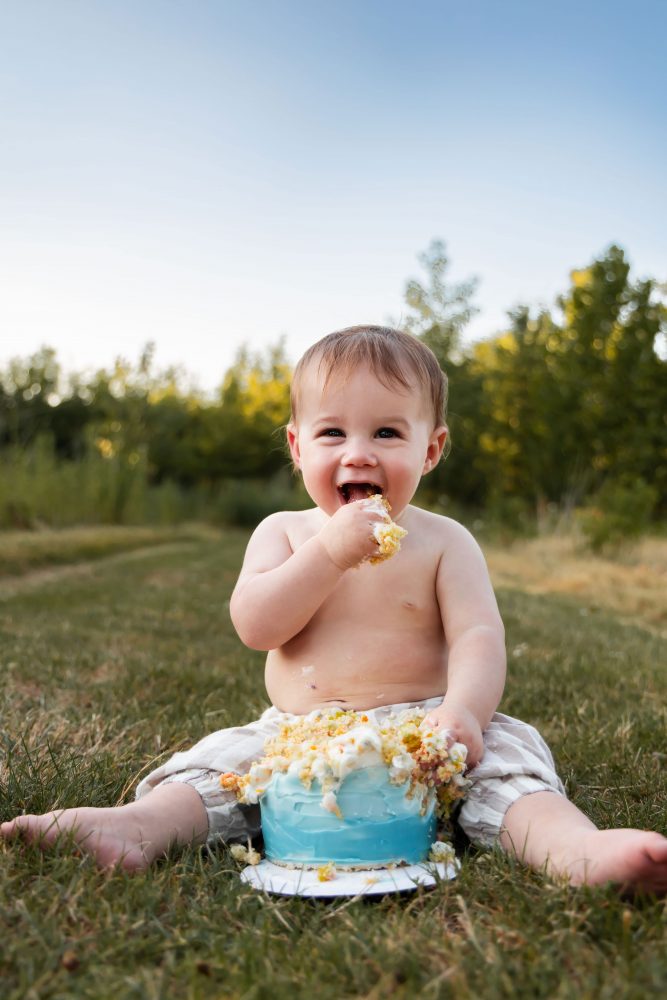 Cleveland cake smash photographer captures a laughing one-year-old covered in birthday cake frosting during an outdoor session.