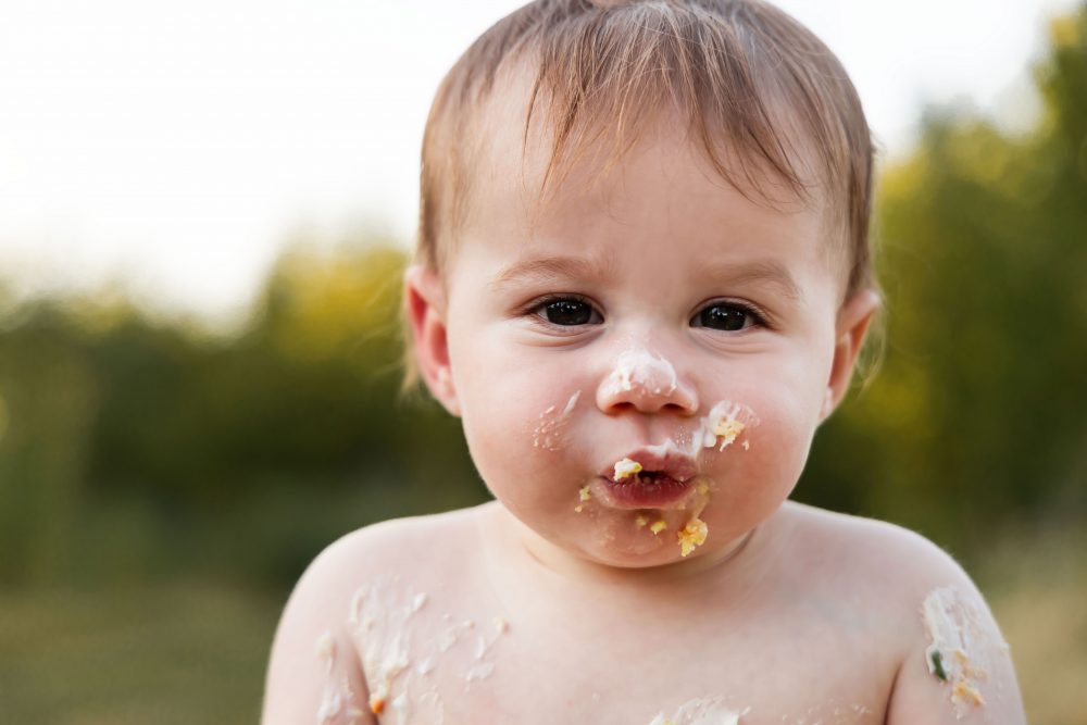 Cleveland baby photographer Allison Liffman captures a playful cake smash moment with a smiling baby covered in frosting.
