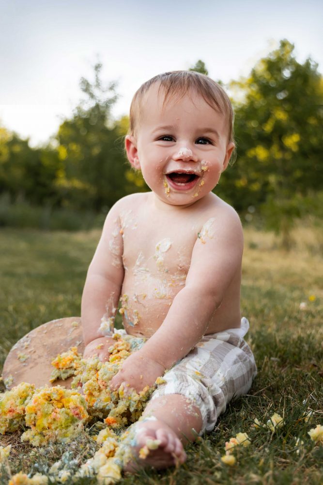 Allison Liffman Photography captures a playful outdoor first birthday cake smash in Cleveland, Ohio, with a smiling baby and colorful cake.