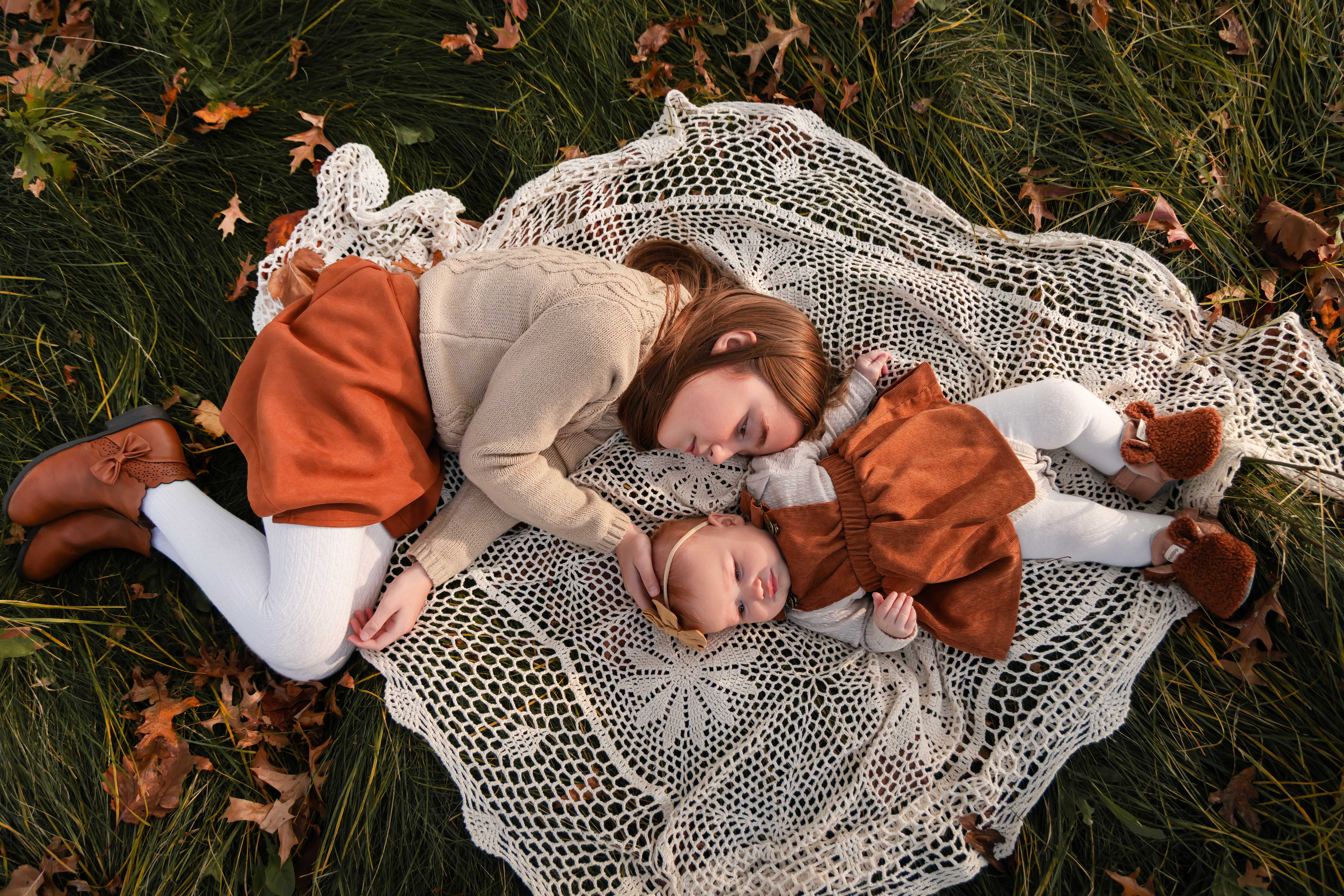 two sisters lay on a blanket in the grass during an outdoor sunset photoshoot with Cleveland, Ohio family photographer Allison Liffman