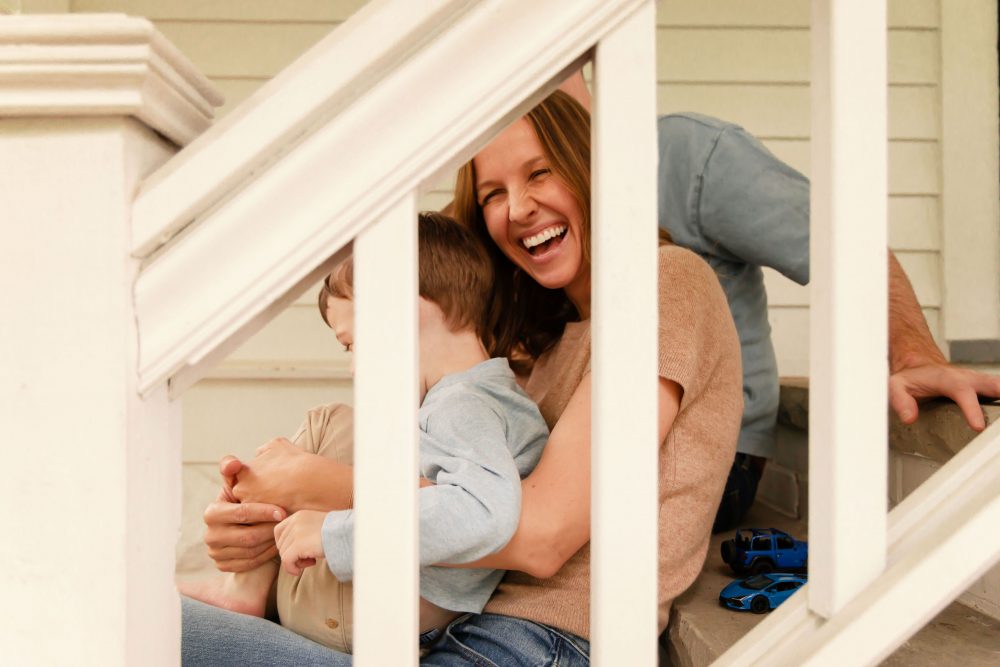 Cleveland family photography capturing a smiling mother cuddling her toddler between white porch railings.