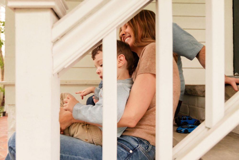 Cleveland family photography capturing a smiling mother cuddling her toddler between white porch railings.