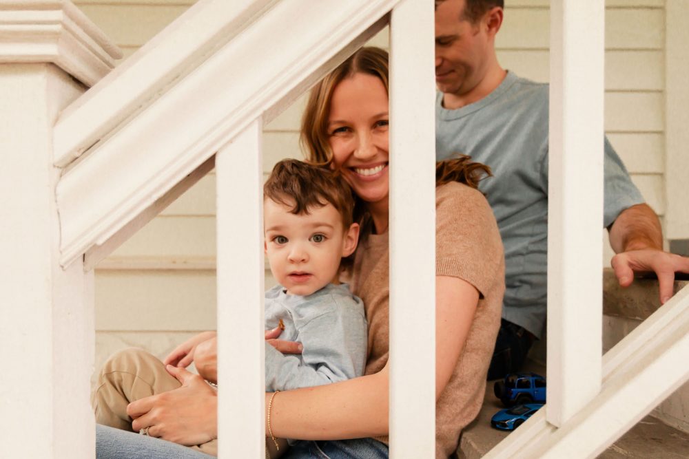 A happy mom holding her young son on the front porch during a lifestyle family photo session.
