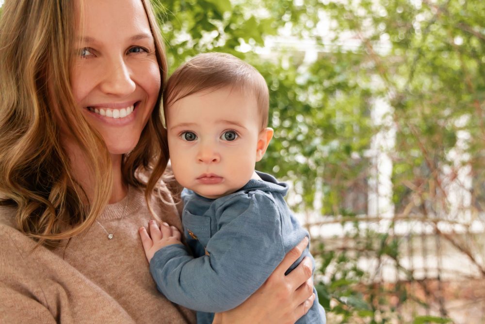 A happy mom holding her young son on the front porch during a lifestyle family photo session.