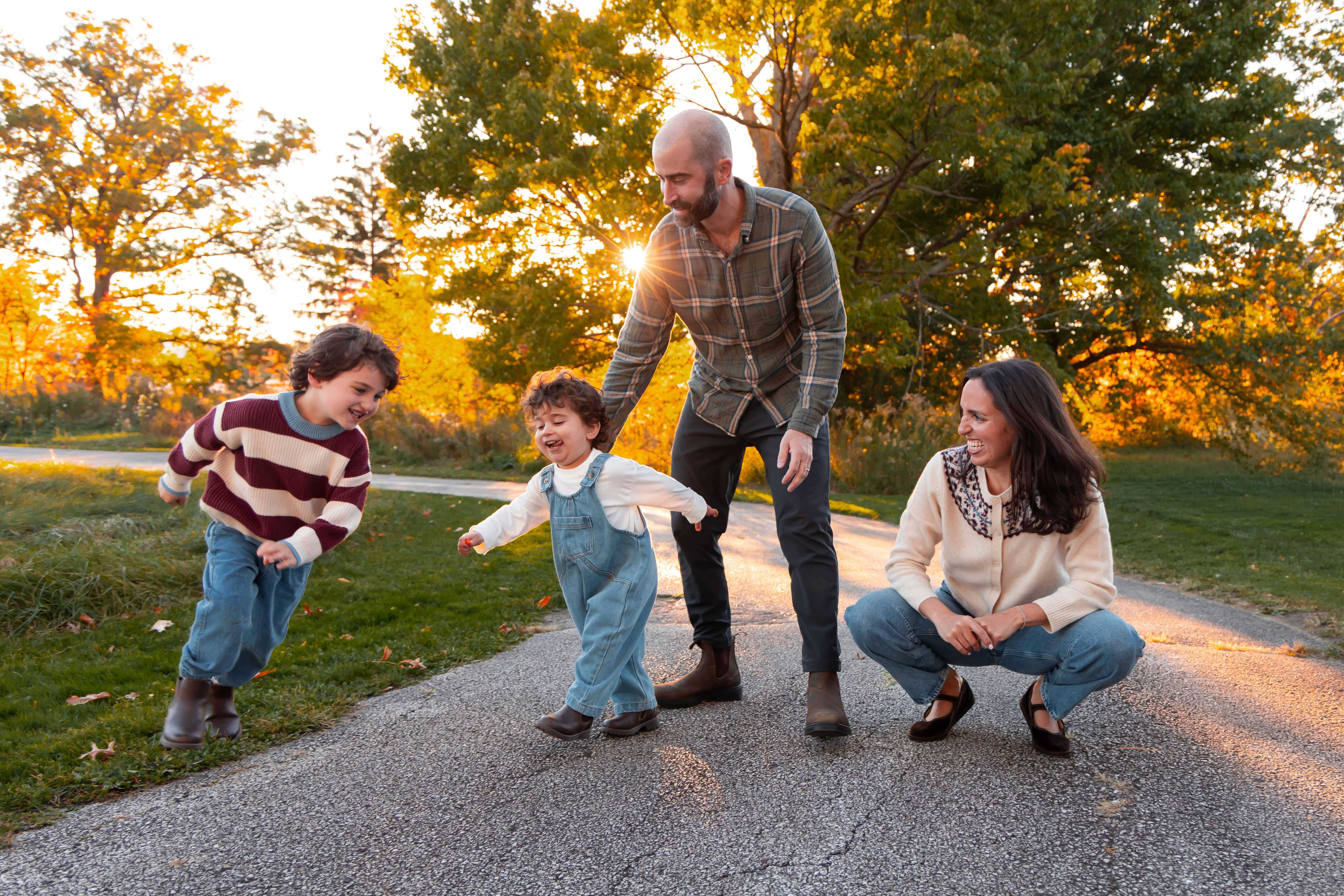 Family of four with two young boys play and run around during an outdoor sunset photoshoot in a park in Cleveland, Ohio.