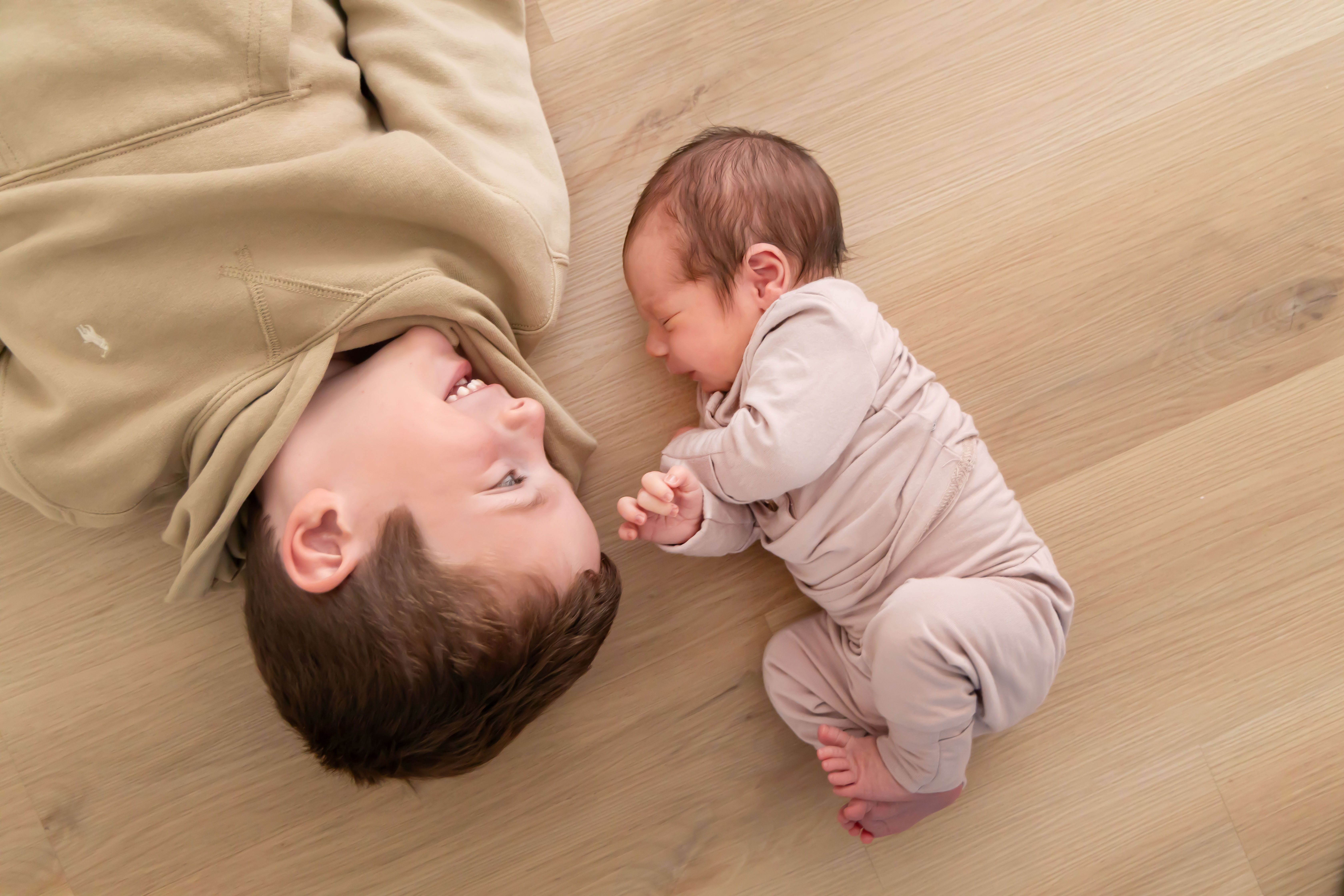 little boy laying next to his newborn baby brother on the floor during an at home natural light family and newborn photography session with Cleveland, Photographer Allison Liffman