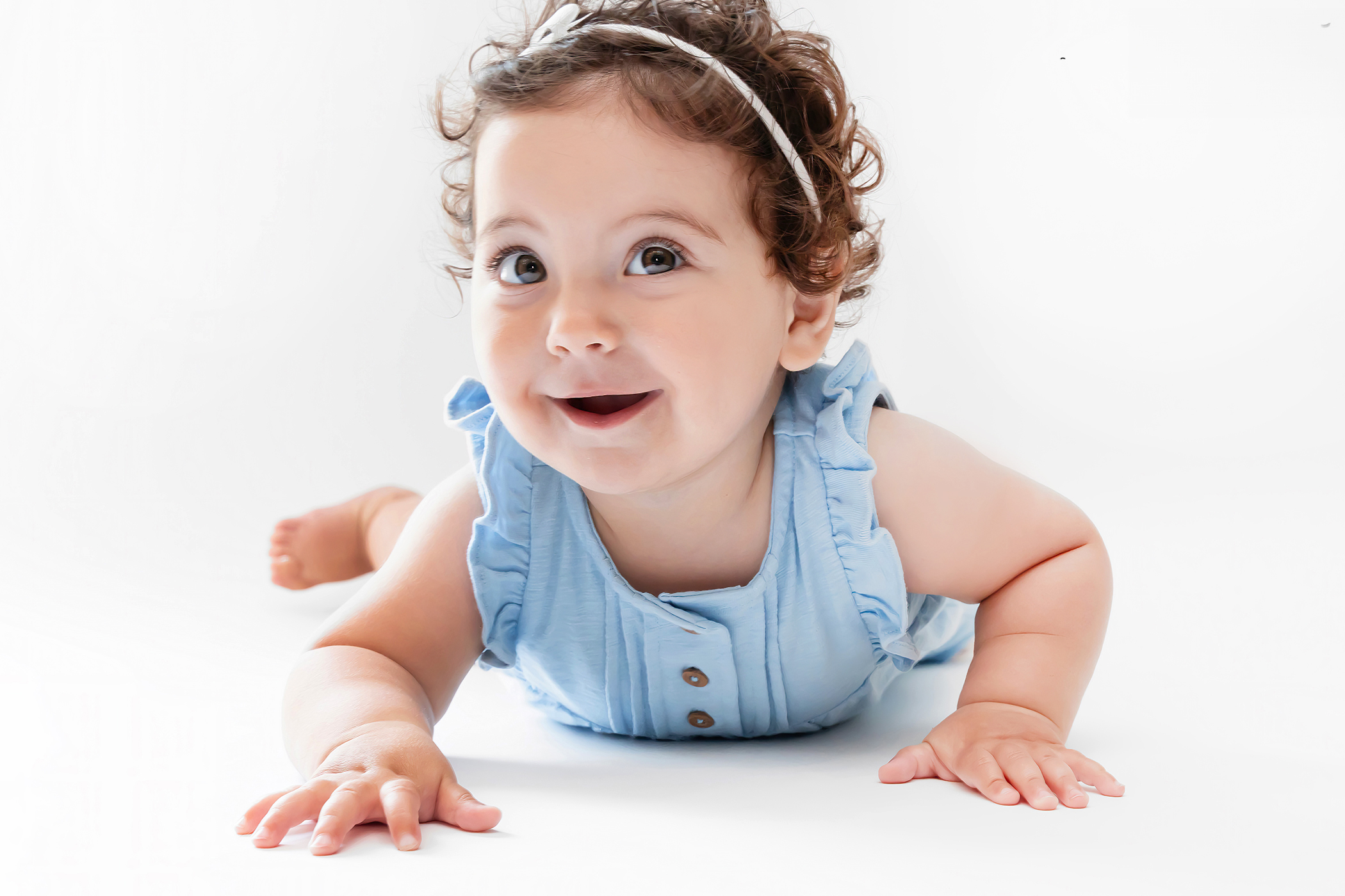 Portrait of a baby girl in blue laughing and crawling on the ground during a studio photoshoot with Cleveland, Ohio photographer Allison Liffman